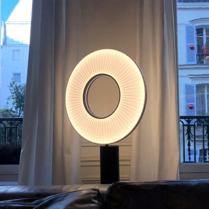 Lampe ronde plissée allumée sur pied noir près d’une fenêtre