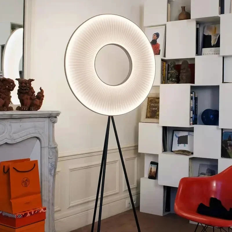 Lampadaire à anneau lumineux plissé sur trépied noir près d’une bibliothèque