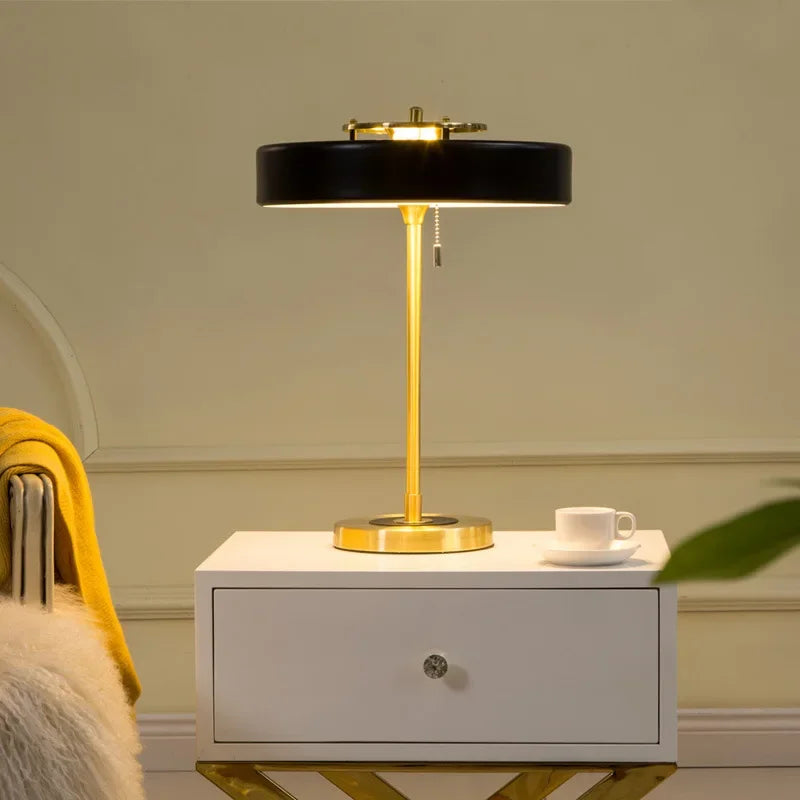 Lampe nordique noire et dorée allumée sur une table de chevet blanche