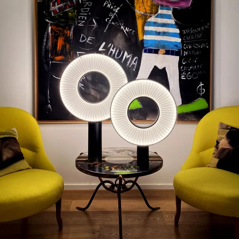 Deux lampes rondes plissées de tailles différentes sur une table entre des fauteuils jaunes