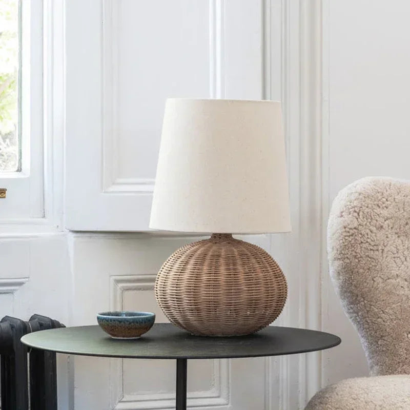 Lampe à pied arrondi tressé sur une table noire près d’un fauteuil